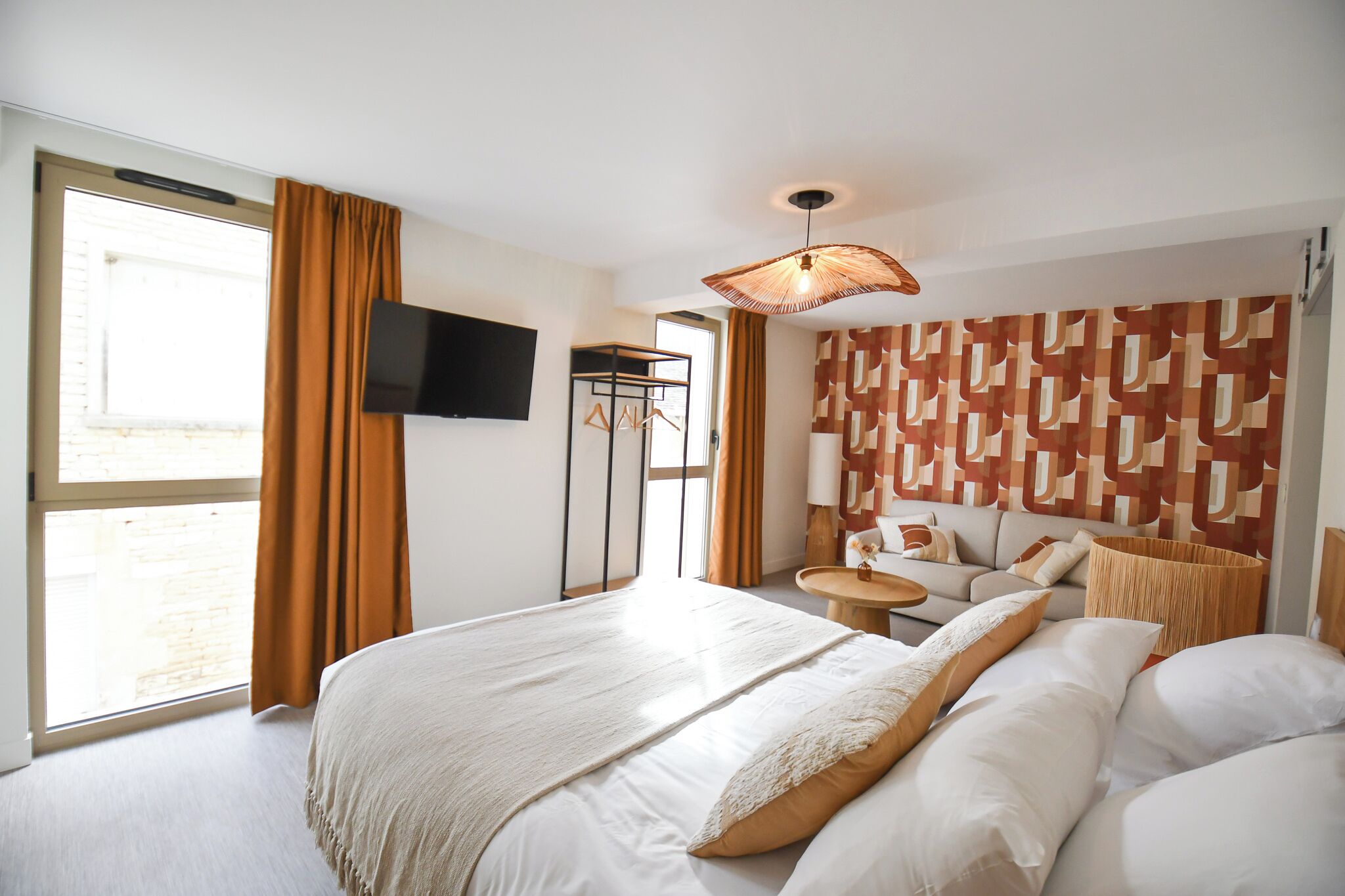 A hotel room with a large bed, a TV mounted on the wall, a sofa, a small table, and a patterned wall.