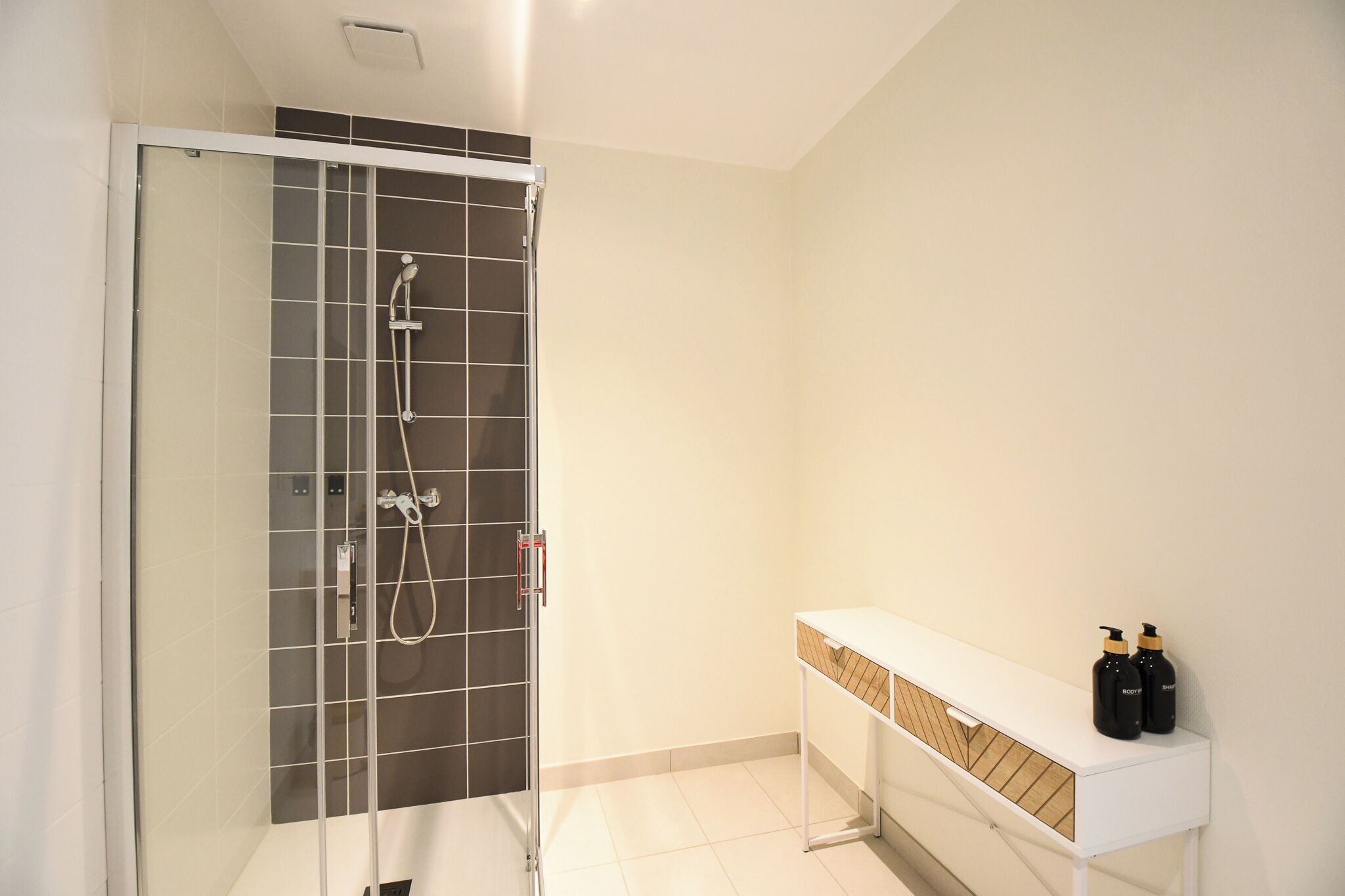 A modern bathroom with a glass-enclosed shower, a white vanity with a wooden tray, and two bottles of lotion on the counter.