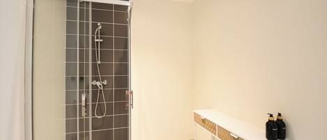 A modern bathroom with a glass-enclosed shower, a white vanity with a wooden tray, and two bottles of lotion on the counter.