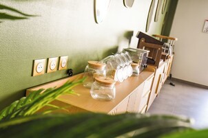 Una barra de madera con frascos de vidrio y una pared verde con textura y enchufes eléctricos.