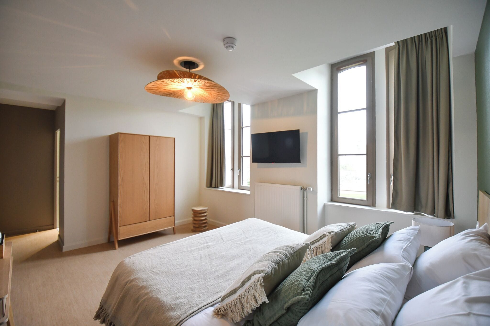 A bedroom with a bed, a TV, a wardrobe, and a window with curtains.
