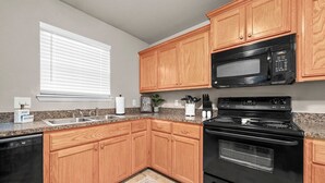 A kitchen with wooden cabinets, a black microwave, a stove, and a dishwasher. -   “Spacious 4-Bed Home: Dual Entrances, Work-Friendly” (Fort Smith)