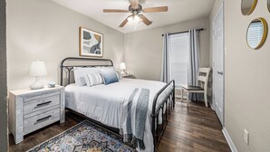 A bedroom with a bed, nightstands, a ceiling fan, a window with curtains, and a door. -   “Spacious 4-Bed Home: Dual Entrances, Work-Friendly” (Fort Smith)