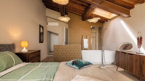 A bedroom with a bed, a nightstand, a lamp, a wooden ceiling, a bathroom with a bathtub, and a shower. - Melaiolo Modern Apartment With Pool Montaione (Montaione)