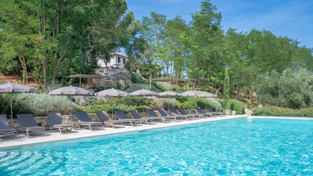 A pool with clear blue water, surrounded by lounge chairs and umbrellas, with trees and a building in the background. - Melaiolo Modern Apartment With Pool Montaione (Montaione)