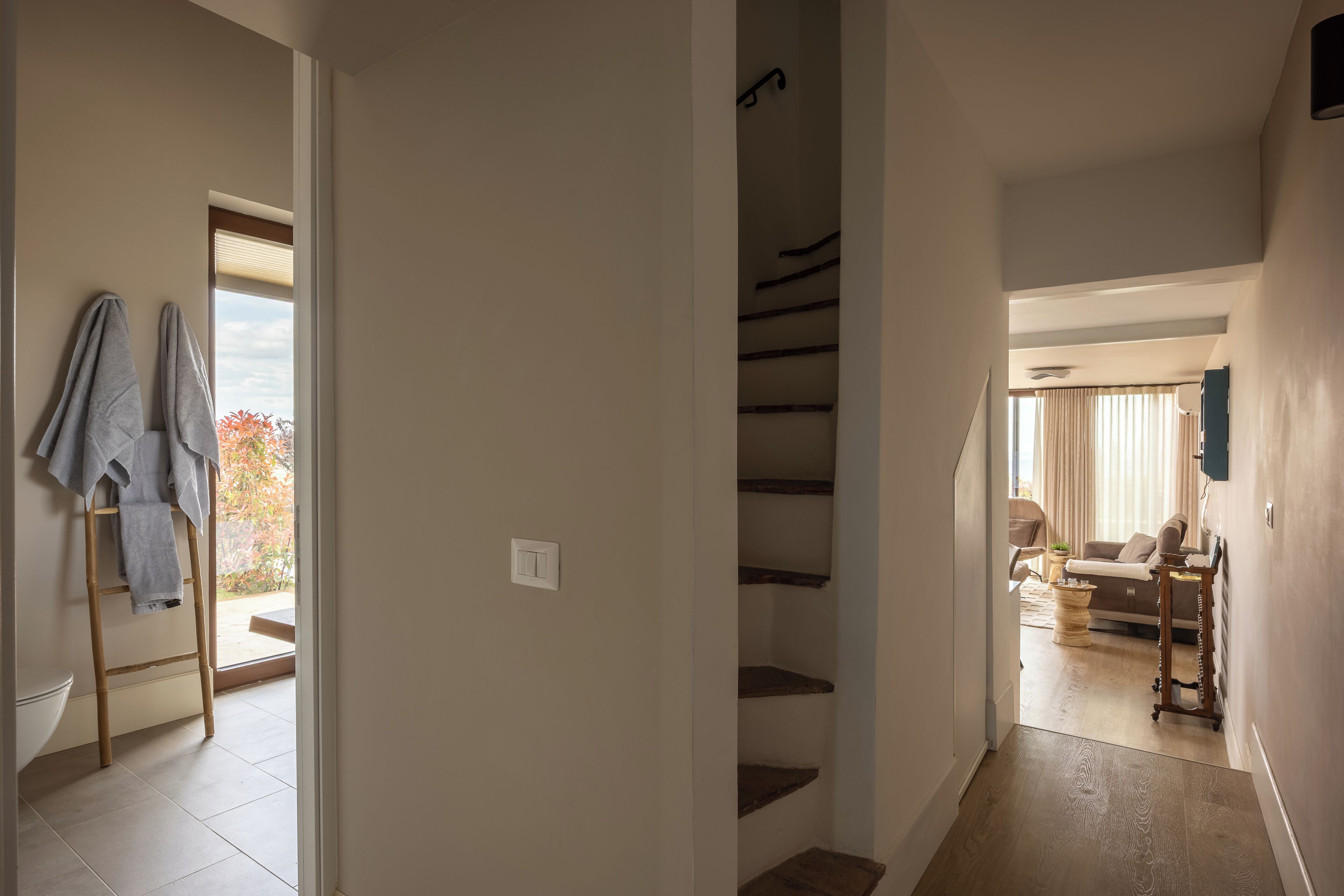 Un pasillo con una escalera, un baño con toallero y una sala de estar con sofá y mesa de centro.