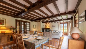 Un comedor con una mesa de madera dispuesta para cuatro personas, rodeada de sillas de madera. Se observa un sofá y un aparador al fondo.