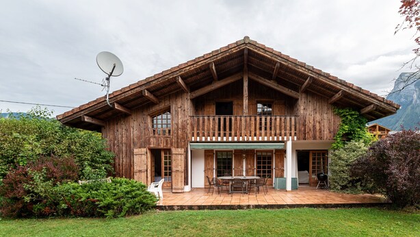 Un chalé de madera con balcón, un patio con mesa y sillas, y una antena parabólica.