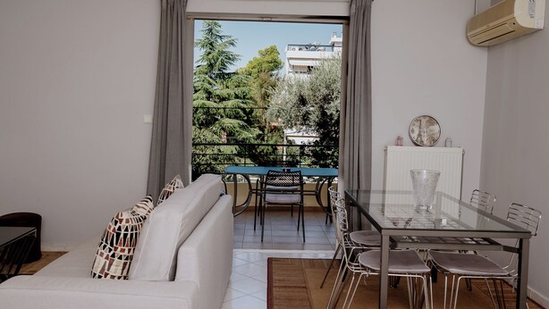 A modern living room with a sofa, a dining table with chairs, and a view of a balcony with a table and chairs.