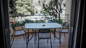 An outdoor balcony with a table and chairs, a view of trees and buildings, and a metal railing.