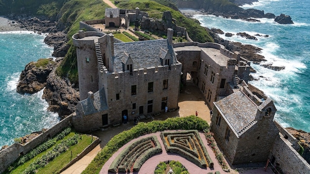 Eine historische Burg aus Stein mit einem Burggraben, gelegen auf einer Küstenklippe mit Blick auf das Meer.