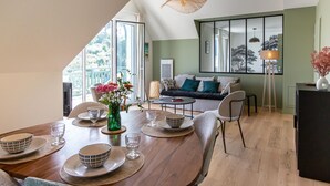 Ein Essbereich mit einem Holztisch, gedeckt für vier Personen, umgeben von Stühlen. Im Hintergrund sind eine Couch und eine Stehlampe zu sehen.