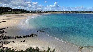 Ein Strand mit klarem türkisblauem Wasser, Sandküste und Häusern im Hintergrund.