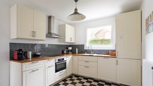 Une cuisine avec des meubles blancs, un carrelage noir et blanc, une fenêtre donnant sur un espace verdoyant et un luminaire suspendu.