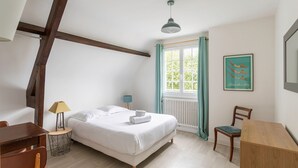 Une chambre à coucher comprenant un lit, un bureau, une chaise, une lampe, une fenêtre avec des rideaux et un tableau encadré accroché au mur.