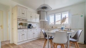 A modern kitchen with white cabinetry, a dining table with chairs, and a unique pendant light. - Ecrin Marin - apt terrasse, bassin d'arcachon (La Teste-de-Buch)