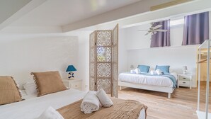 A modern bedroom with a large bed, a nightstand, a decorative screen, and a second bed in the background. - Ecrin Marin - apt terrasse, bassin d'arcachon (La Teste-de-Buch)