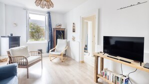 A modern living room with a large window, a wicker ceiling light, a flat-screen TV, a bookshelf, and a wooden coffee table. - Les Brises Normandes - Entre mer, falaises et GR21 (Saint-Pierre-en-Port)