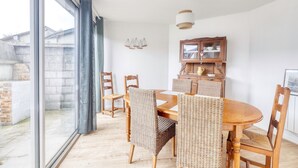 A dining area with a wooden table and wicker chairs, a cabinet with glass doors, and a view through large windows. - Les Brises Normandes - Entre mer, falaises et GR21 (Saint-Pierre-en-Port)