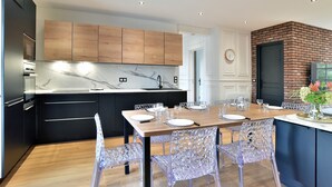 Una cocina moderna con armarios de madera, encimera de mármol y un comedor con sillas traslúcidas.