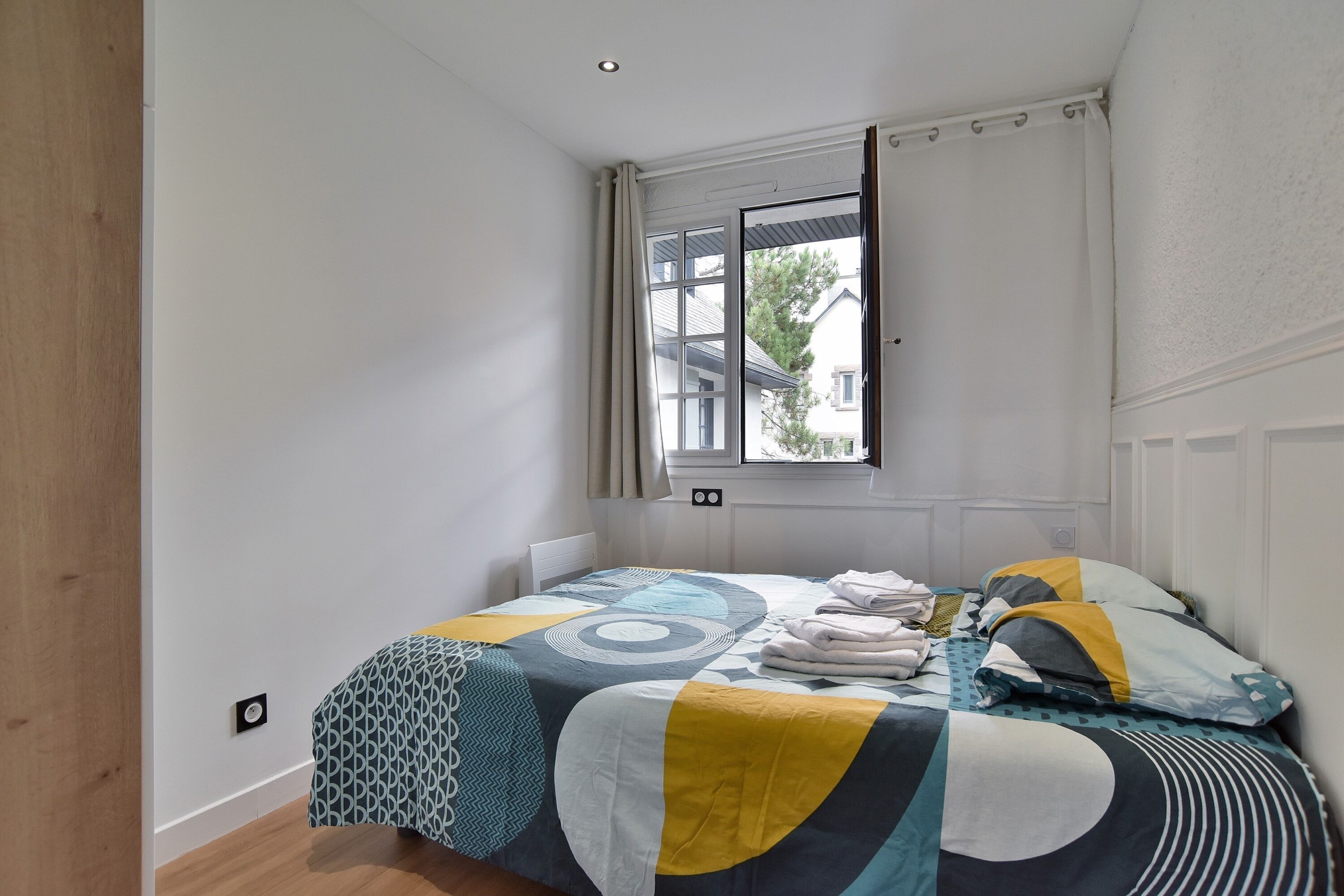 Een slaapkamer met een bed, een raam en uitzicht op een huis.