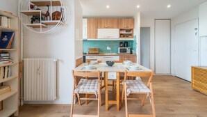 A modern kitchen with wooden cabinets, a white countertop, and a dining area with a table and chairs. - Blue Light - Appt pour 4p, Paris (Paris)