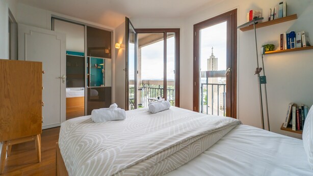 A hotel room with a bed, a wooden wardrobe, a bathroom with a shower, and a balcony with a view of a building. - Blue Light - Appt pour 4p, Paris (Paris)