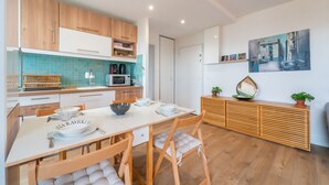 A modern kitchen with wooden cabinets, a white countertop, and a dining area with a white table set for two. - Blue Light - Appt pour 4p, Paris (Paris)