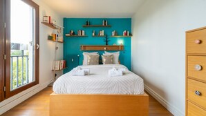 A bedroom with a large bed, wooden headboard, and built-in shelves with books. - Blue Light - Appt pour 4p, Paris (Paris)