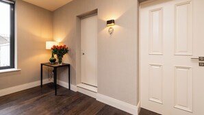 A hallway with a wooden floor, a wall-mounted lamp, a vase with flowers, and a door. - Spacious 1 Bed Loft Apartment in Dublin City Centre (Dublin)