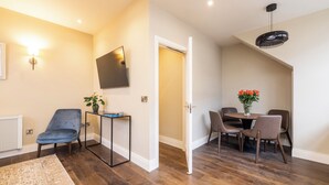 A modern living room with a blue chair, a small table with a plant, a dining area with a table and chairs, and a TV mounted on the wall. - Spacious 1 Bed Loft Apartment in Dublin City Centre (Dublin)