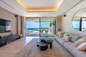 A modern living room with a sofa, coffee table, TV, and a view of the ocean.