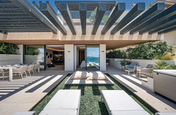 A modern outdoor pool area with lounge chairs, a dining setup, and a view of the sea.