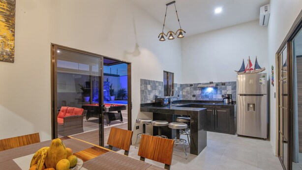 A modern kitchen with a built-in island, stainless steel appliances, and a pool area visible through glass doors. - La Casa de Papi (Parrita)