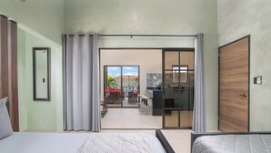 A modern hotel room with a large bed, a desk with a chair, and a sliding glass door leading to a balcony with outdoor seating. - La Casa de Papi (Parrita)