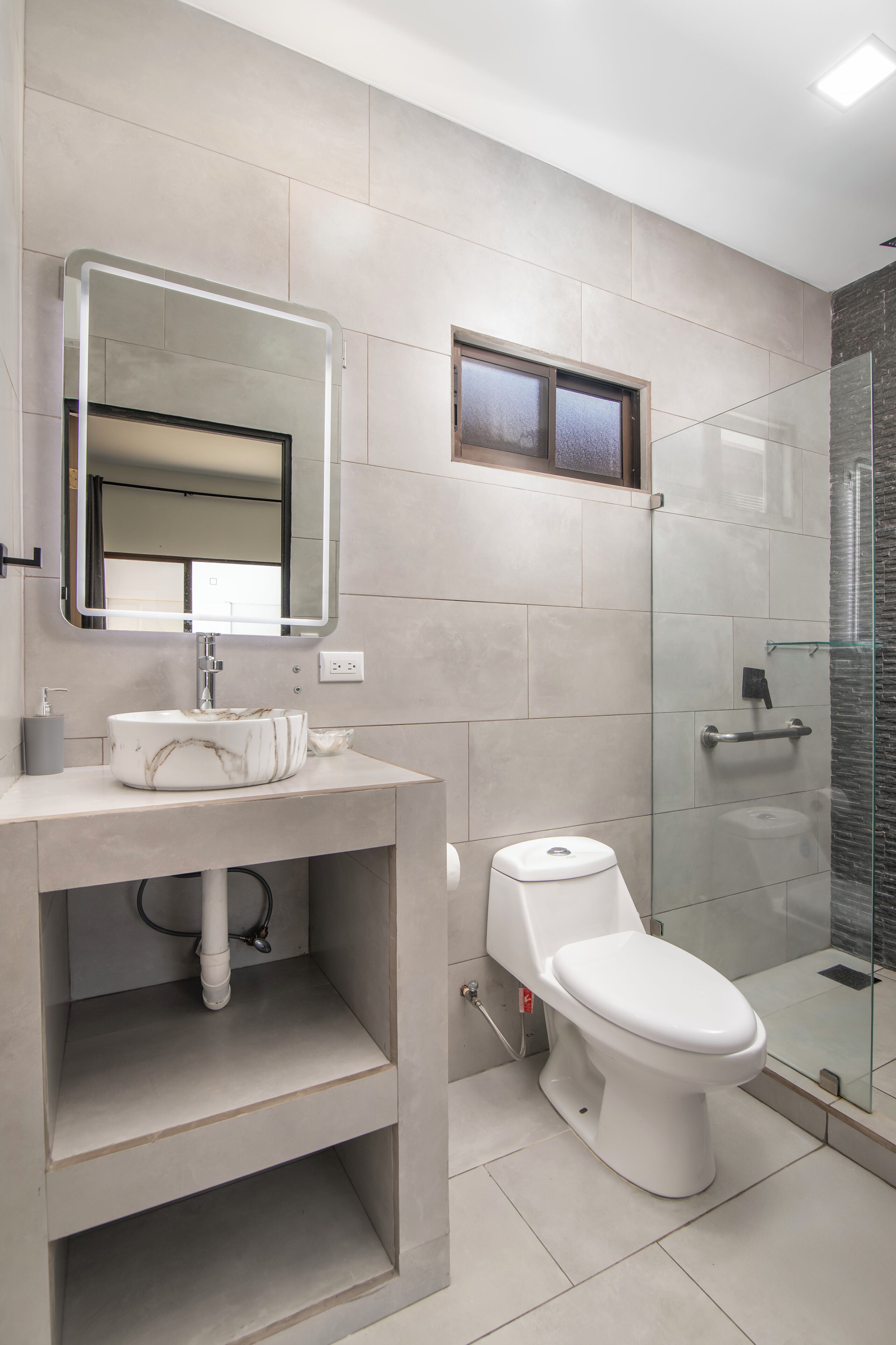 Een moderne badkamer met een marmeren wastafel, een douchecabine van glas en een toilet.