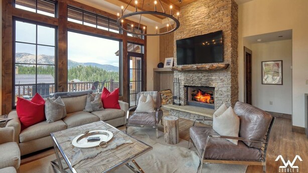 A spacious living room with a stone fireplace, large windows, and a cozy seating area. - The BEST Ski In/Out! Immediately next to Montage! (Big Sky)