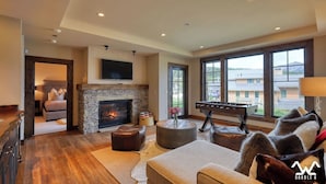 A spacious living room with a fireplace, a foosball table, and a large window offering a view of the surrounding area. - The BEST Ski In/Out! Immediately next to Montage! (Big Sky)