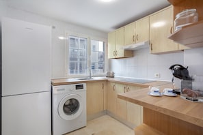 A modern kitchen with wooden cabinets, a built-in washing machine, and a window providing natural light.