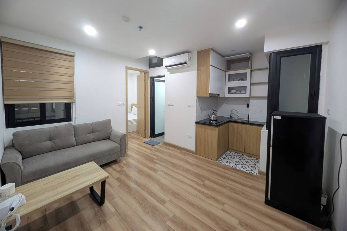 A compact living space with a sofa, a small table, a kitchenette with a sink and stove, and a black refrigerator.