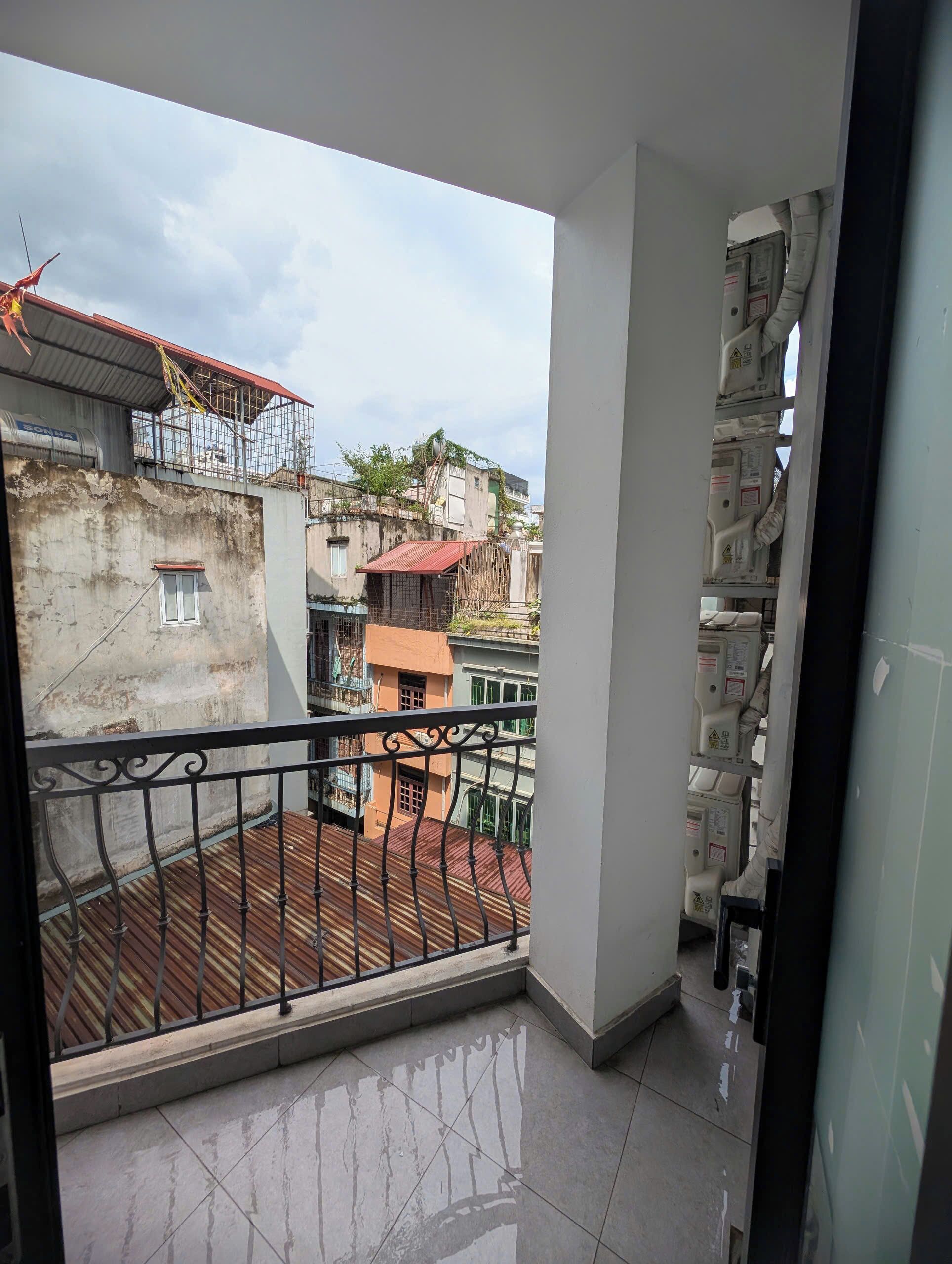 Un balcón con barandilla de metal, suelo de baldosas y vista a edificios cercanos.
