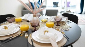 Una mesa de comedor dispuesta con platos blancos, cubiertos dorados y copas de vidrio rosa, junto con jugo de naranja.