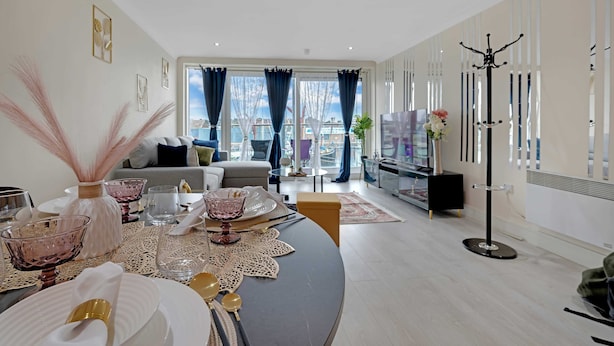 Una sala de estar moderna con comedor, ventanas grandes con cortinas, un sofá y un televisor.