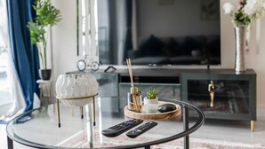 Una sala de estar moderna con una mesa de centro de vidrio, televisión y objetos decorativos.