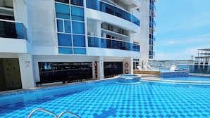 A swimming pool with a blue checkered pattern, surrounded by a building with balconies and a view of the sea. - PARCEROS GROUP - 2 BEDROOM VACATION APARTMENT, 14TH FLOOR, CARTAGENA, SPAIN (Cartagena de Indias)