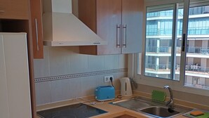 Une cuisine avec des meubles de rangement en bois, un four encastré, une cuisinière, un évier et une fenêtre donnant sur des immeubles.