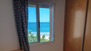 Une chambre à coucher avec un lit, une commode en bois, une fenêtre donnant sur la plage et un rideau.