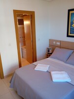 A bedroom with a bed, a nightstand, a lamp, and a door leading to a bathroom.