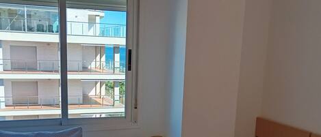Una habitación de hotel con dos camas, una mesita de noche con lámpara y ventana con vistas a un edificio.
