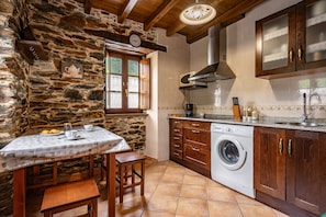 A rustic kitchen with stone walls, wooden cabinets, a washing machine, and a dining area with a table and chairs. - Apartment 'Mira' with Mountain View, Private Terrace and Wi-Fi (Boal)